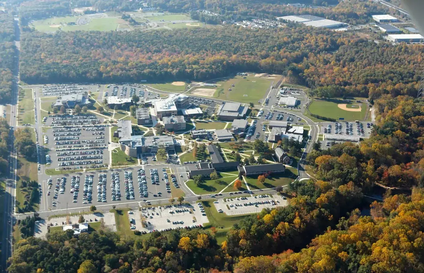 Aerial view of a campus with multiple buildings, large parking lots, and athletic fields surrounded by forest, representative of the environments maintained by Camden County painters.